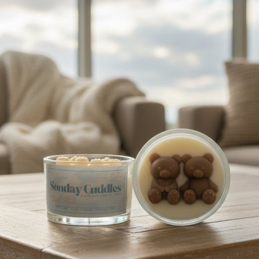 A wickless candle shown open next to its lid, labeled 'Sunday Cuddles' by Soft Touched. The candle wax inside is pale cream, and the lid features two small brown teddy bear figures molded into the wax.